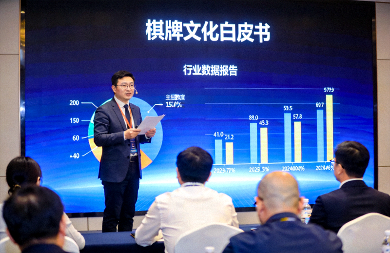 棋牌文化白皮书发布会现场，讲者在深蓝色背景屏幕前向观众解读行业数据报告